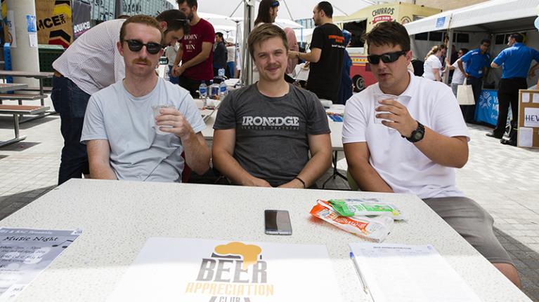 three male students host a beer appreciation club stall at orientation