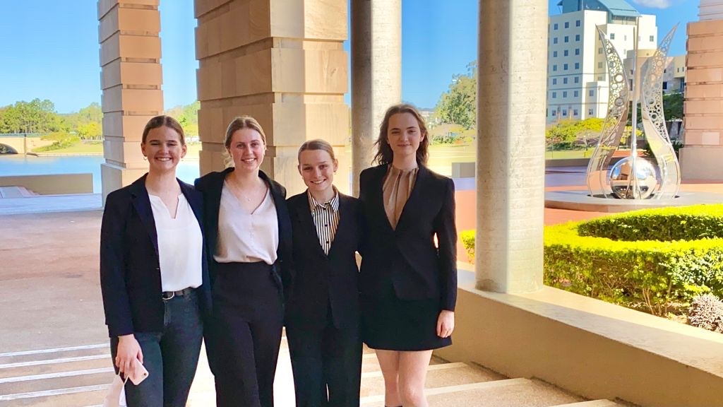 4 young female university students in professional dress, with blue skies and sandstone in the background