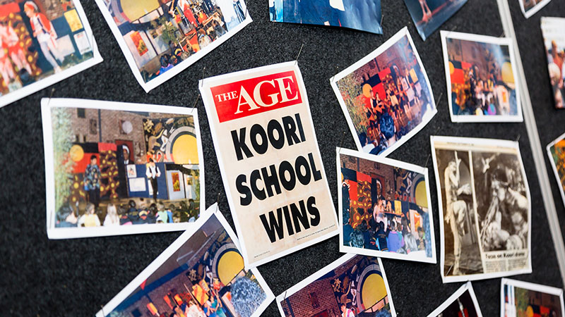 A series of posters and photos on a wall. The middle one is a newspaper headline that reads 'The Age: Koori school wins'