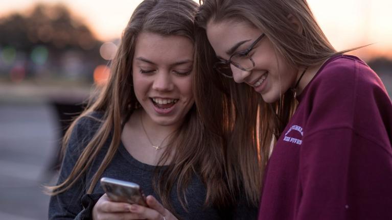 two teenage girls smiling at smart phone