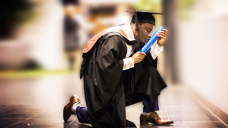 Mlisho Karega kneeling and kissing his graduation certificate