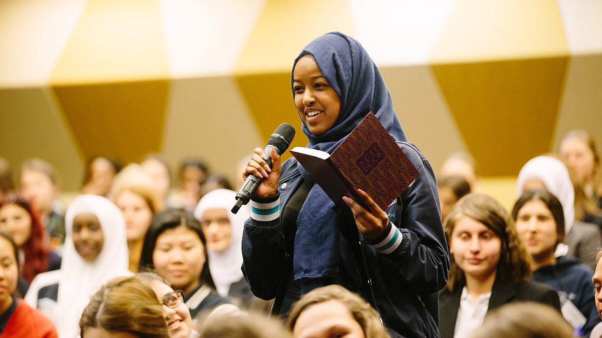Young African-Australian woman in a hijab speaks into a microphone in a large auditorium
