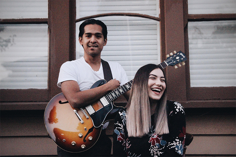 Young man of latino appearance, holds guitar, with pretty young woman smiling broadly