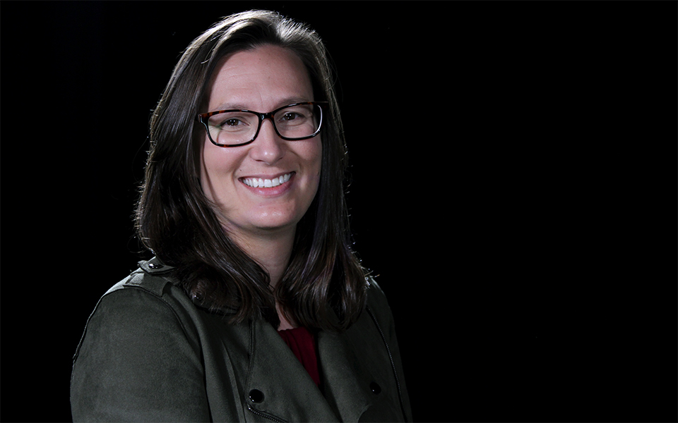 A woman wearing glasses smiles at the camera