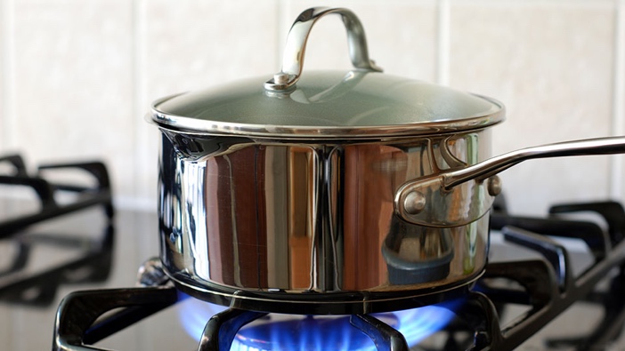A saucepan sits over an open flame on a gas stove.
