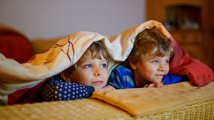 Two kids hide under a doona watching TV.