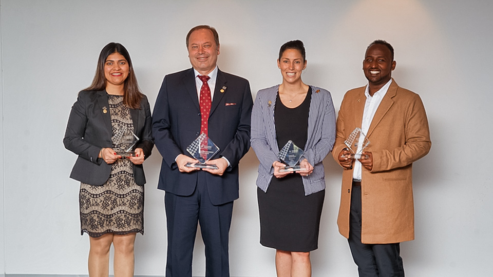 A multicultural group of men and women, in their 30s–50s, hold glass awards