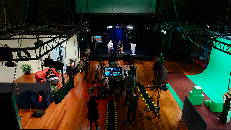 Top-down view of tv studio being used, with cameras, lights and green screens.