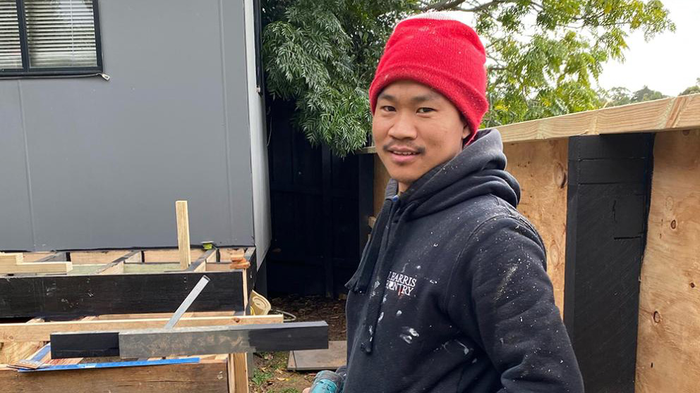 Khamh on a job site, drill in hand as he pauses to pose happily