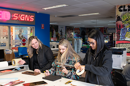 Chloe alongside two female students working in the signs and graphics space