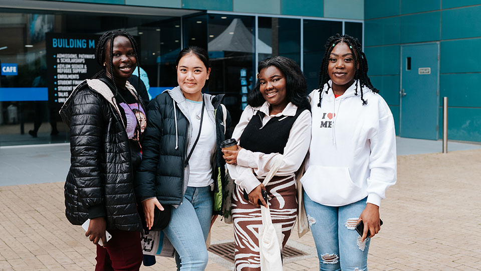 Four prospective students pose for a photo outside Building M at Footscray Park on VU's 2023 Open Day.