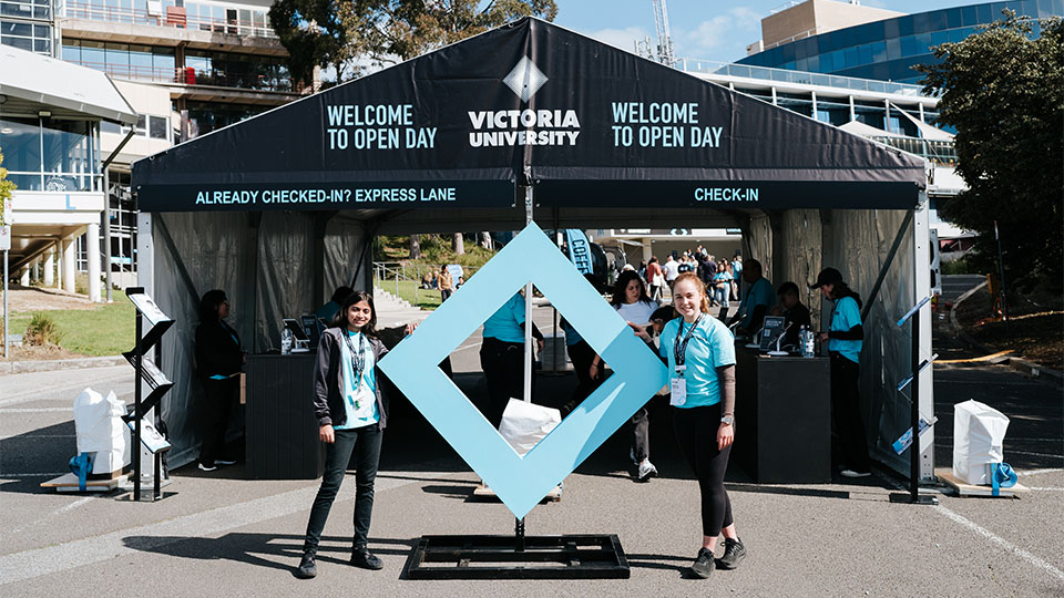 Two students stand either side of a replica of the VU blue branded diamond at Open Day, 2023, Foostcray Park.
