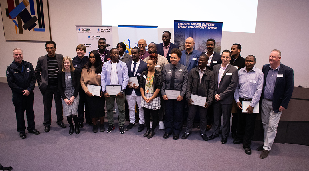A multicultural group holding certificates, flanked by police