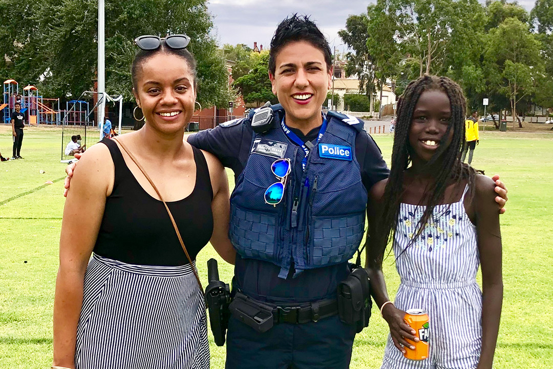 A policewoman in uniform with fair skin smiles with a woman and girl of African appearance