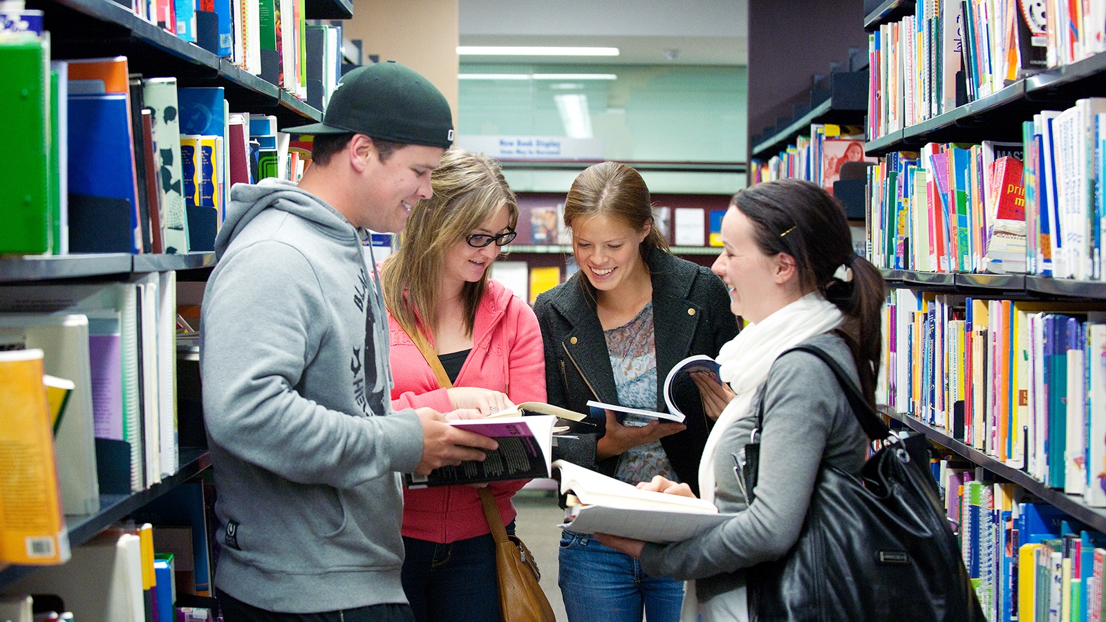 A group of students with open books in their hands, discussing in the library