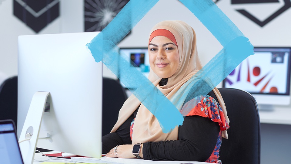 Person sitting at a computer, looking at the camera and smiling.