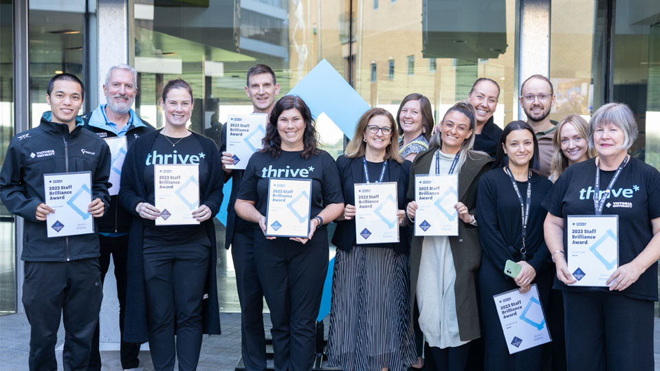 Thirteen representatives from the Thrive team smile at the camera, holding their awards for the Innovation category.