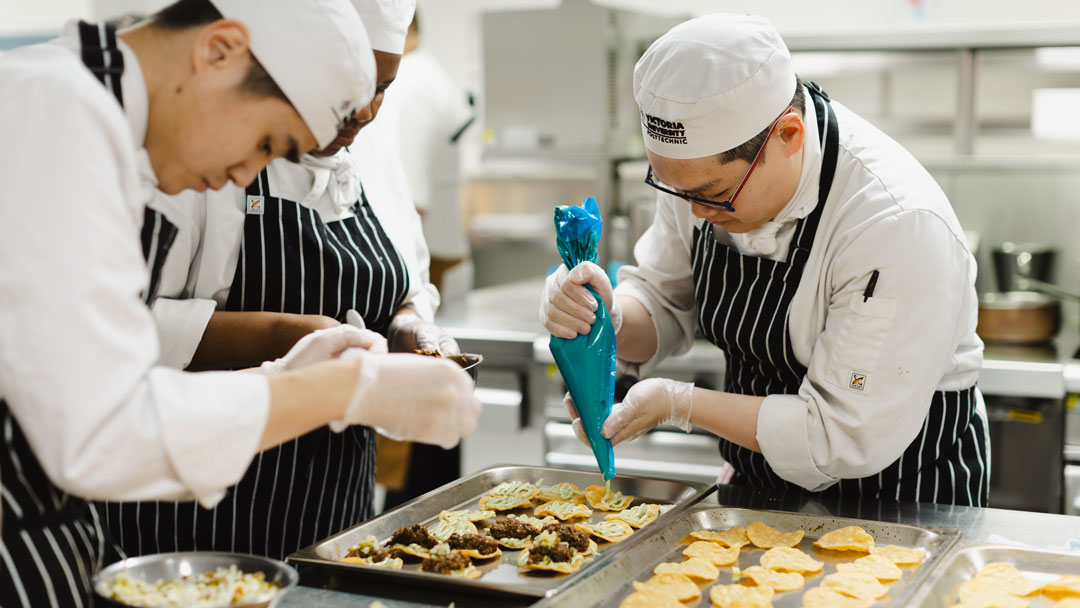 Student chefs preparing a dish. One is squeezing a piping bag.