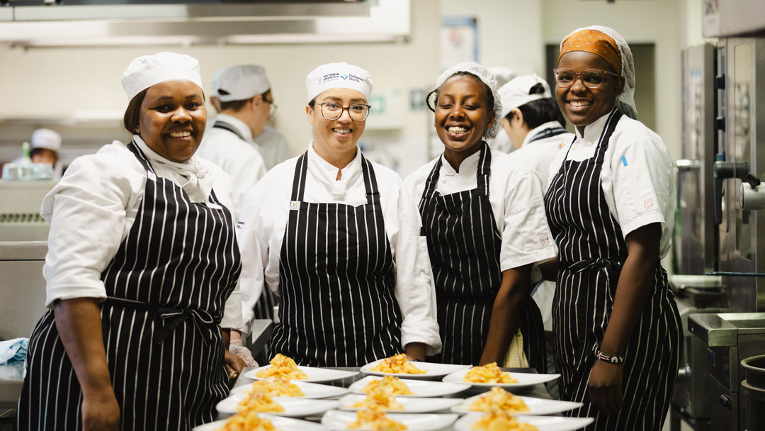 VU student chefs standing behind a set of prepared dishes, smiling at the camera