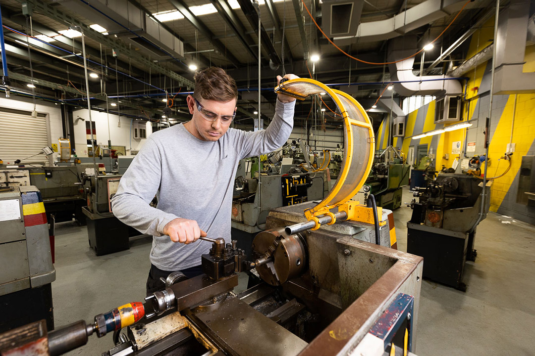 A young man operates sophiticated machinery in a large, bright workshop