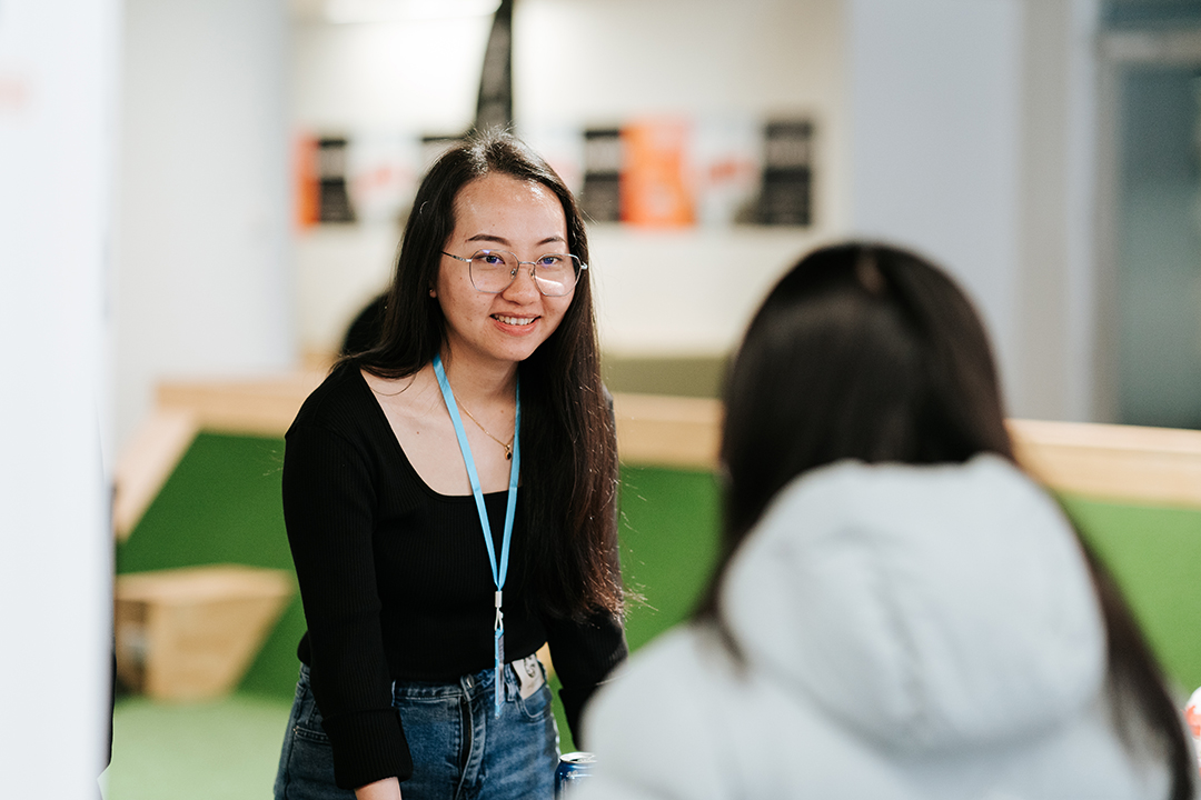 A young woman with a lanyard talks to a student in a bright, modern room