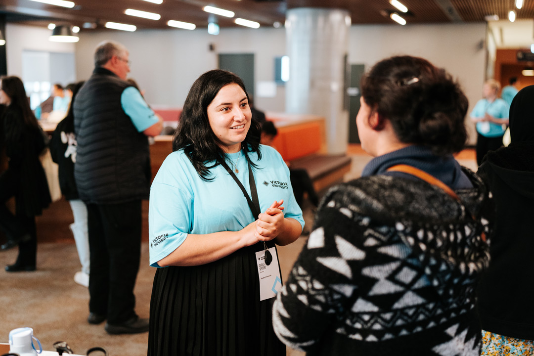 A smiling woman in a Victoria University t-shirt and lanyard helps with information