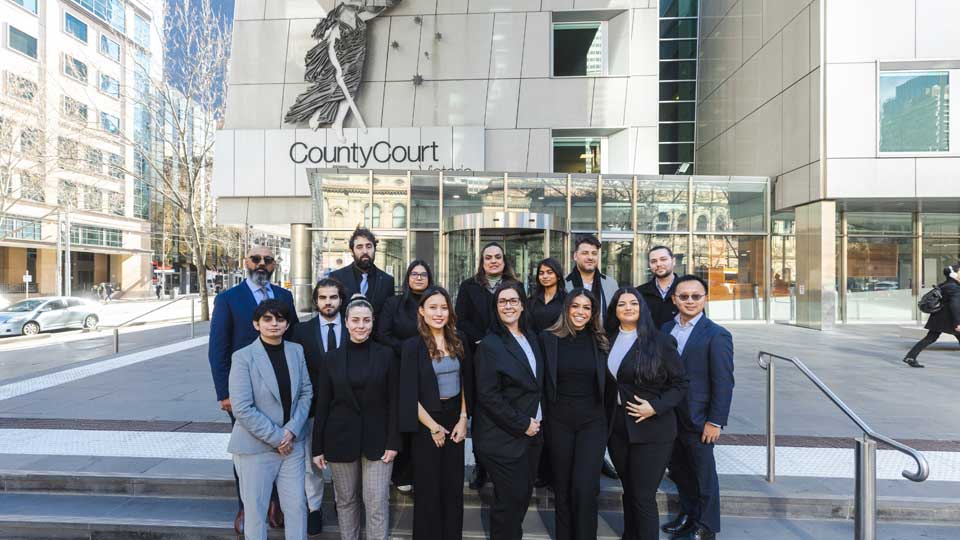 A group of 15 barrister shadowing program participantx, standing and smiling on the steps outside the County Court.