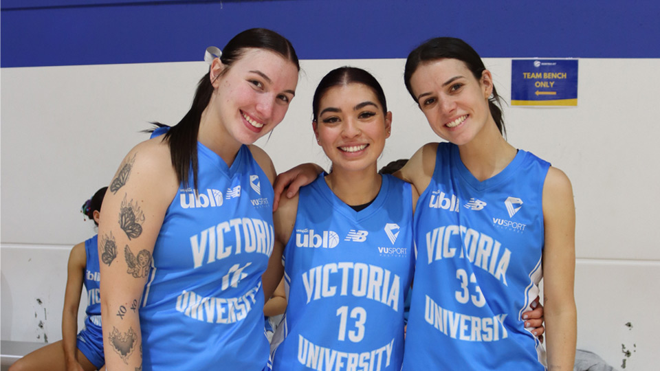 Three players in the VU Vultures womens basketball team smile at the camera, courtside at UniSport Nationals 2024