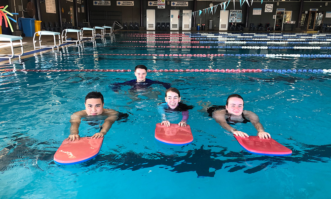 three young adult swimmers learning to swim using flutter boards