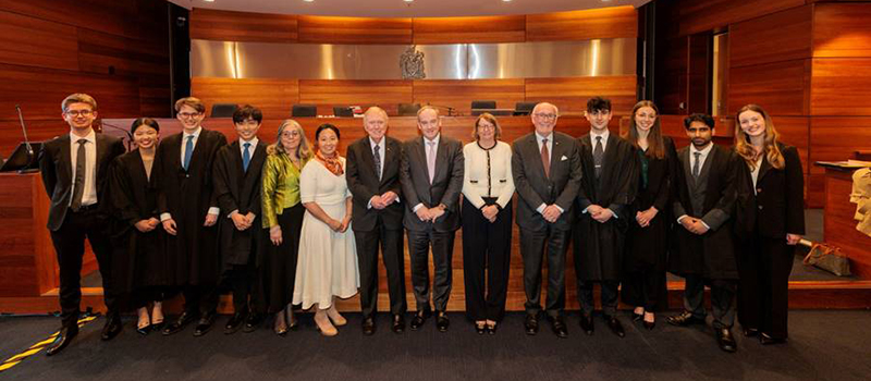 A group of students and professionals pose in suits in a formal court room