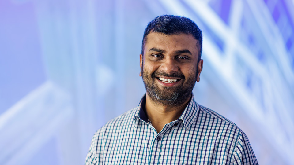 Professor Malindu Sandanayake smiling at the camera in front of an abstract image of a construction site 