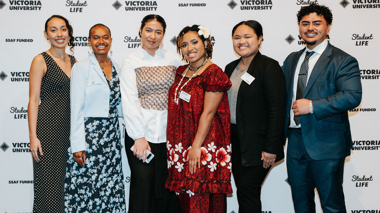 Students standing in front of a VU backdrop, smiling for camera.