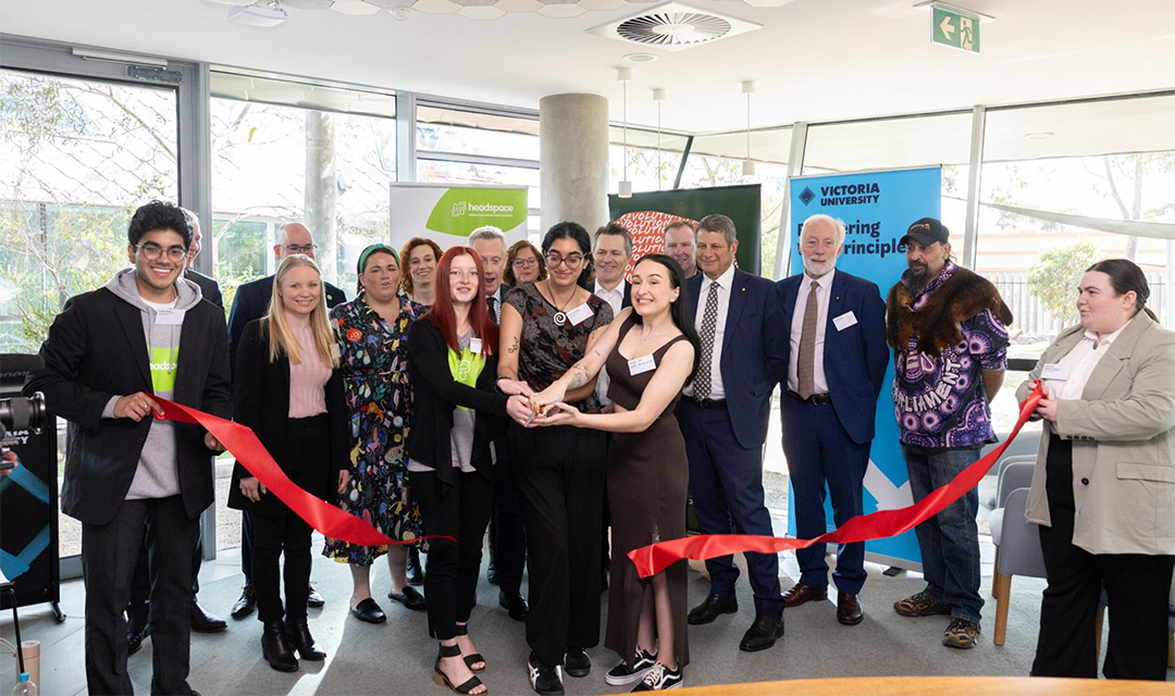 A room full of people celebrate by cutting a red ribbon in front of Victoria University Partners branded banner