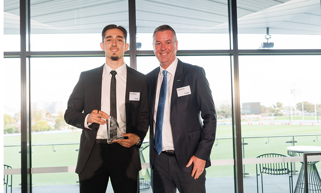 A young man in a suit holds an awards, posing with a middle-aged man