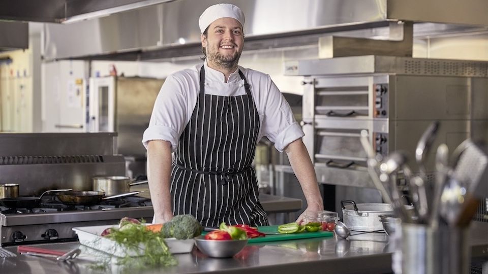 Vu student chef stands in front of chopping board with vegetables placed in front of them.