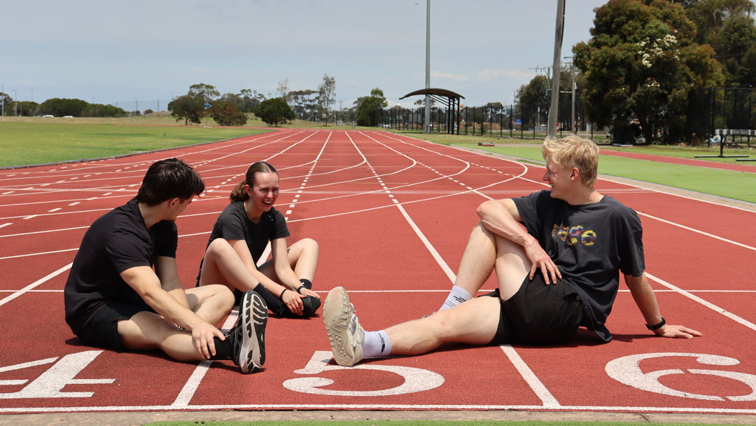 Three students sitting on an outdoor athletics track.
