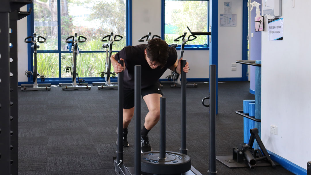 A person pushing a gym sled with weights on it.