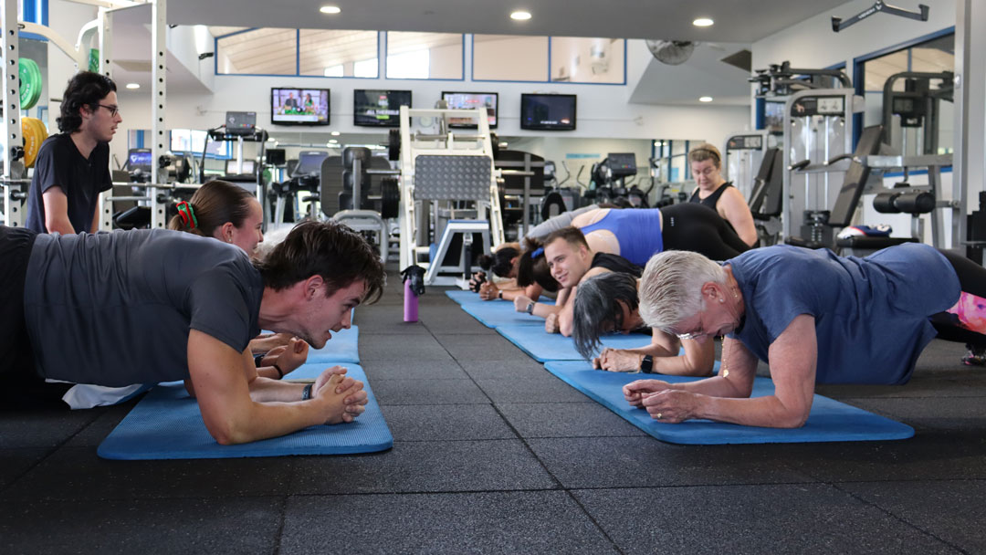 A group of people doing crunches on a yoga mat in a gym.