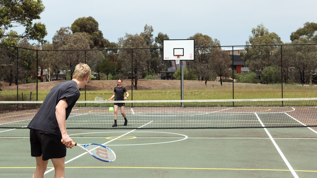 Two students playing tennis on an outdoor court.