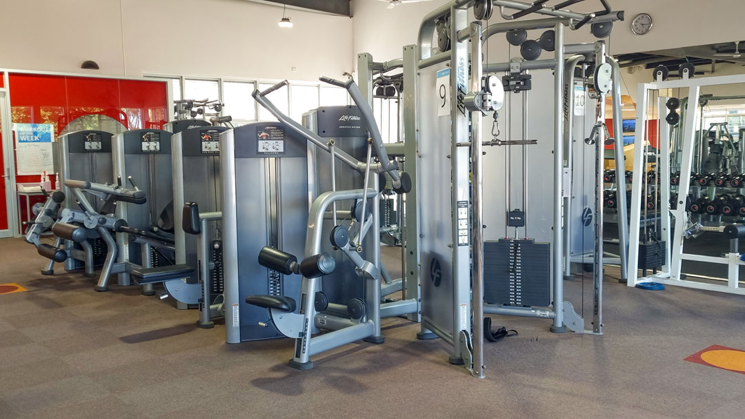 A gym floor with training machines and dumbbells.