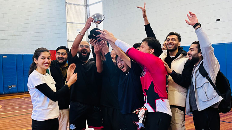 A group of students on a basketball court. One student holds up a trophy, and the other students celebrate around them.