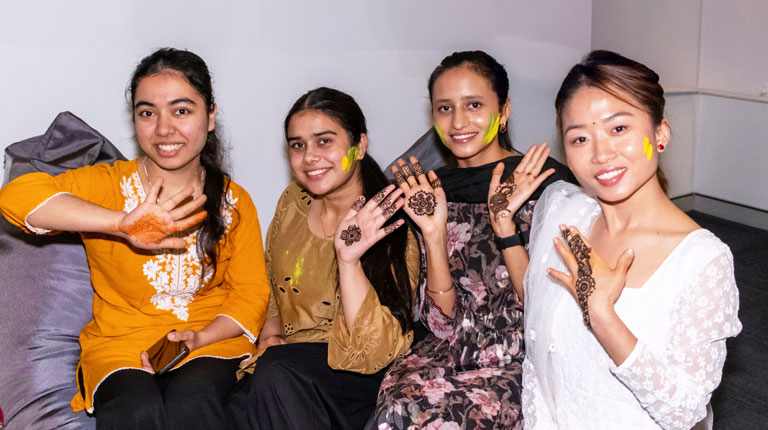 Four students with coloured paint on their cheeks and hands as part of Holi Festival.