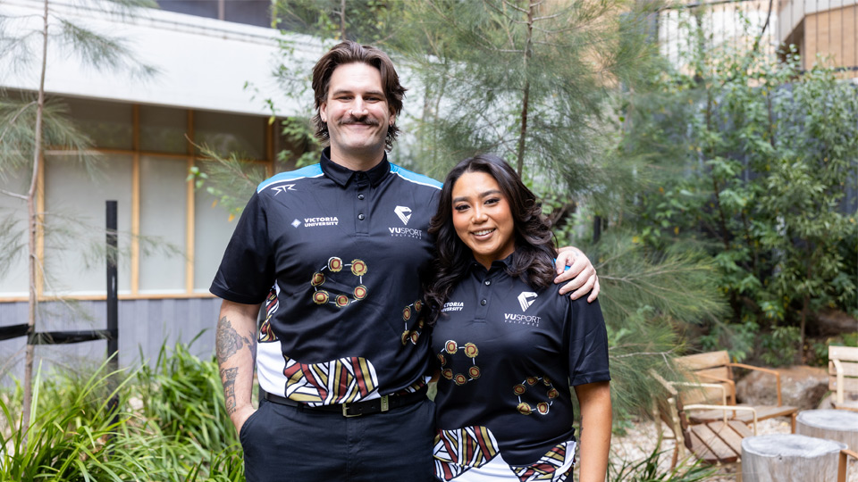 Adam and Stella stand together in the Moondani Balluk garden in their team jerseys. They both smile at the camera.