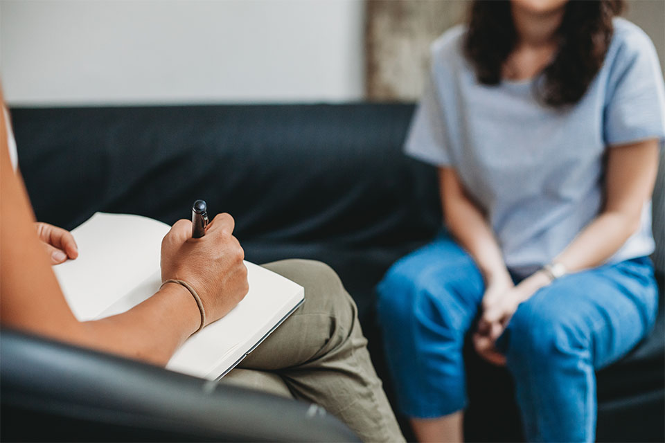 A counsellor writes down notes while listening to a patient sat across from them.