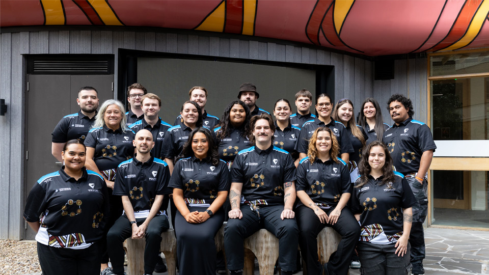VU Moondani Balluk squad and support team before the 2025 Indigenous Nationals. A group of 20 people sit and stand for a team photo in the Moondani Balluk garden at VU Footscray Park.