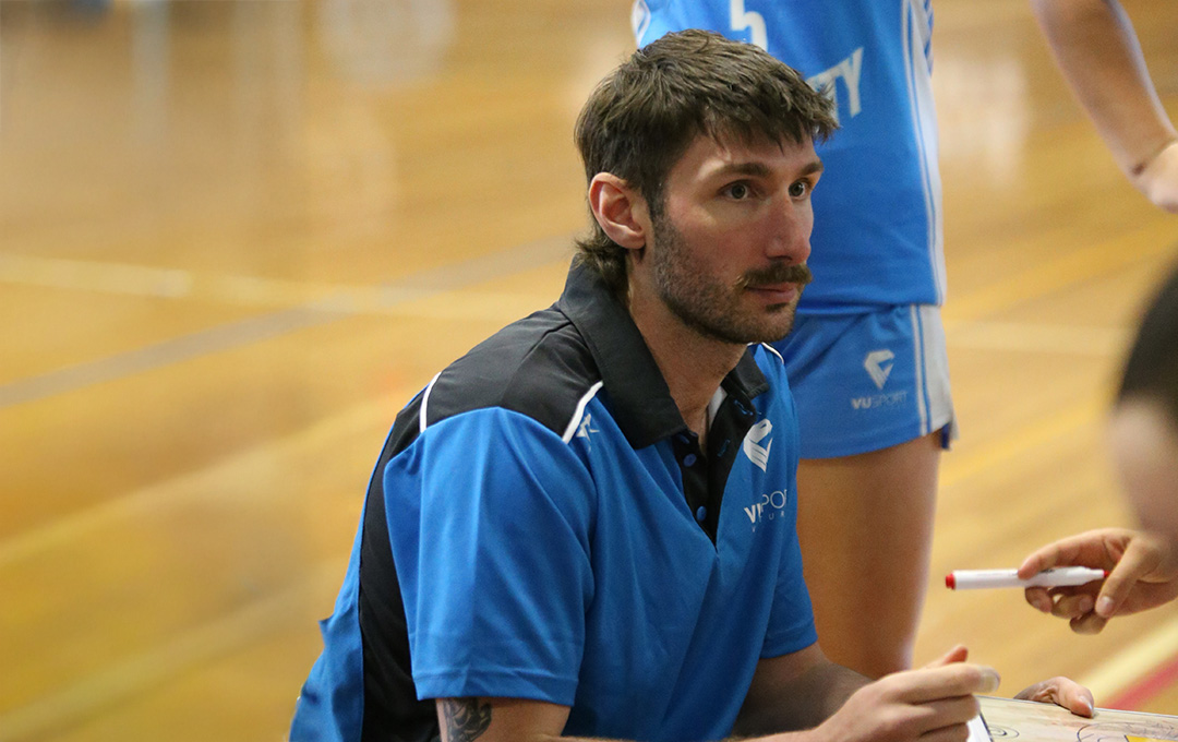 A young man in a VU blue sports uniform makes notes at a basketball court