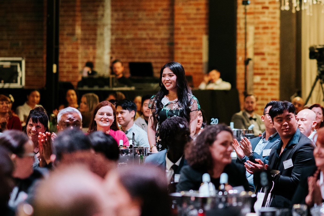 A large, warm, vibrant room full of people seated at tables and smiling