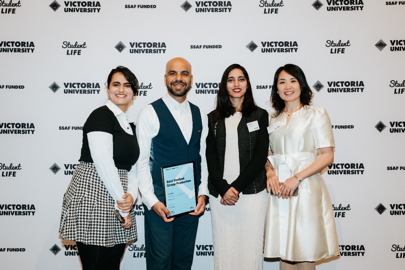 A multicultural, formally dressed group of men and women pose with an award