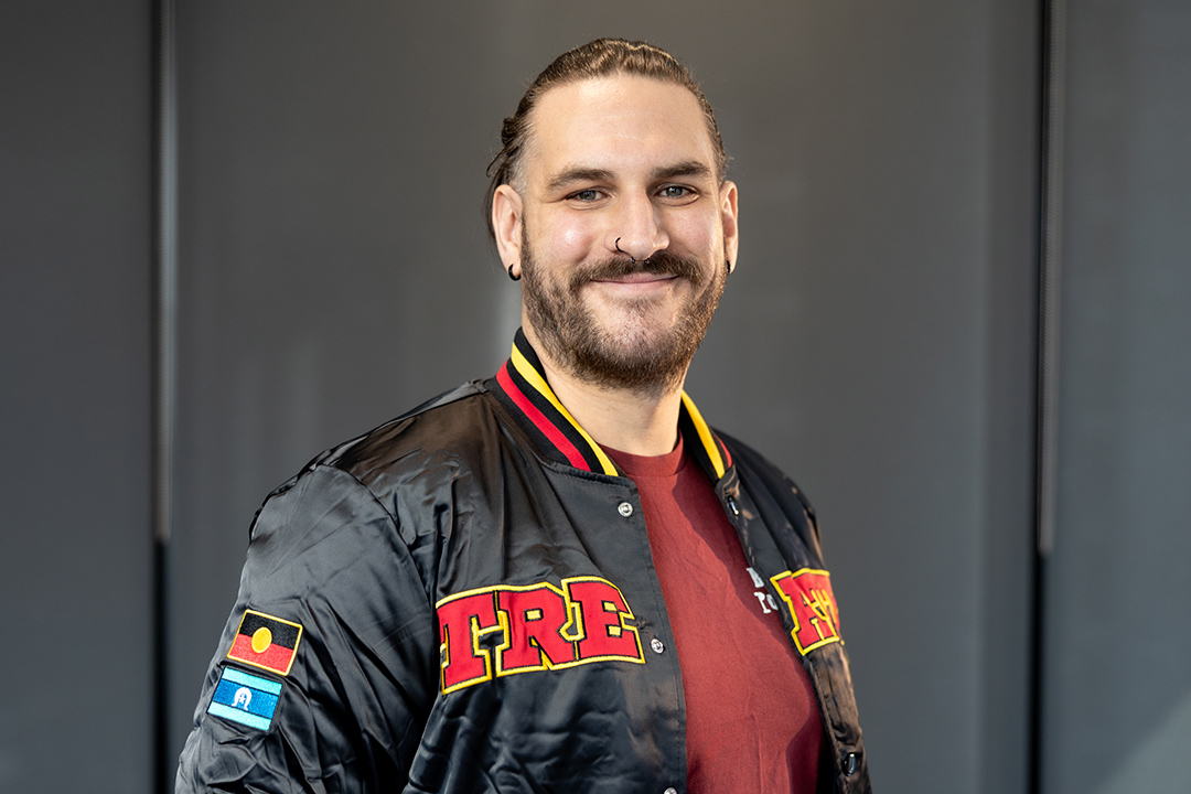 A young man poses in a jacket with the Aboriginal flag on the sleeve