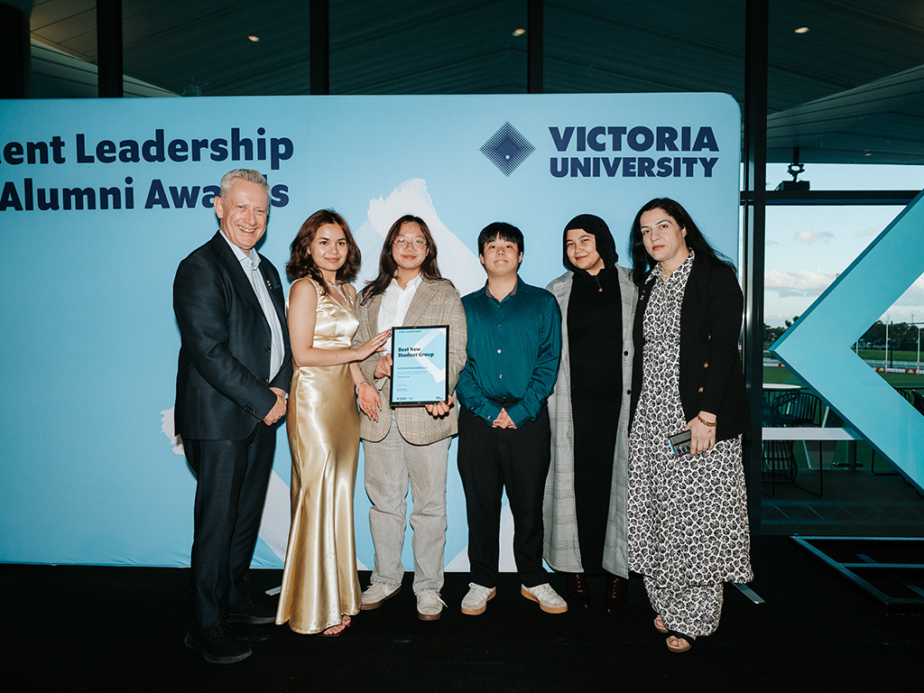 A group of young people pose with the VC against a Victoria University backdrop